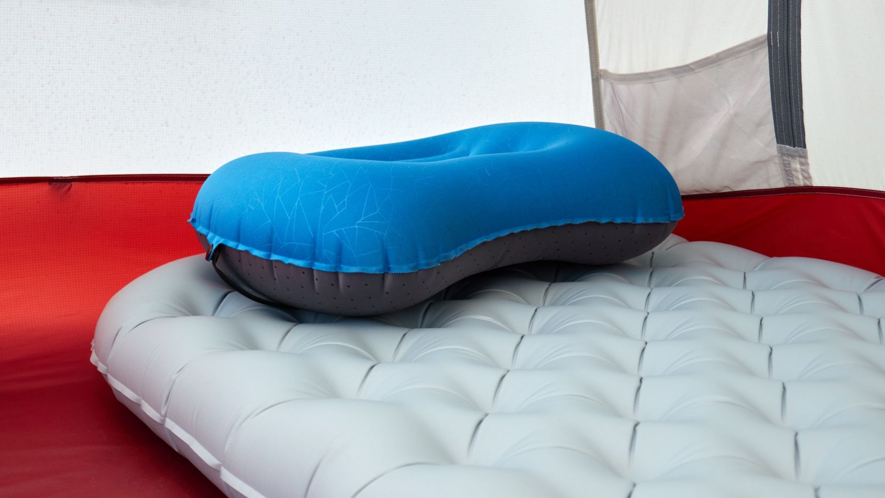 A blue inflatable pillow rests on a light gray quilted sleeping pad inside a tent.