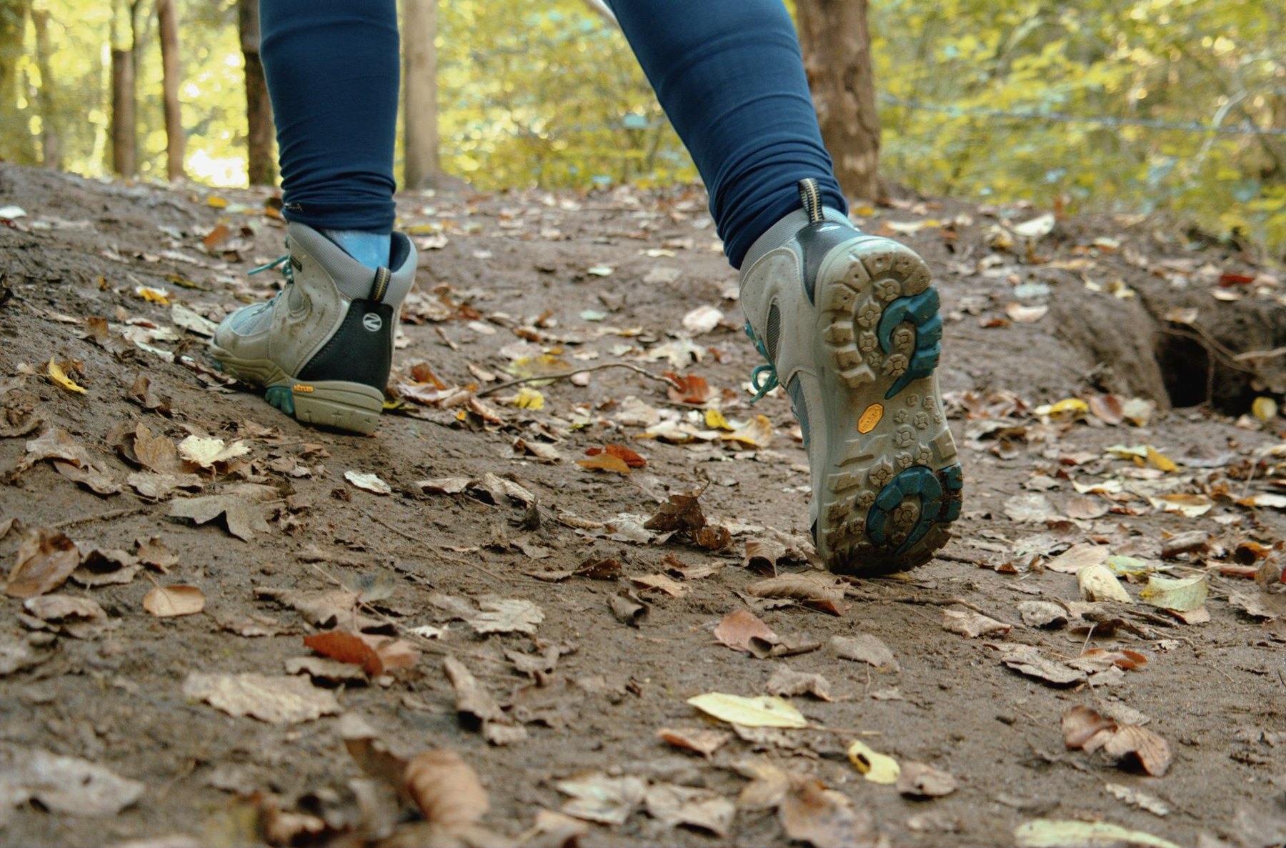 Close-up of a hiker’s footwear on a leaf-covered woodland slope, with one sole visible.