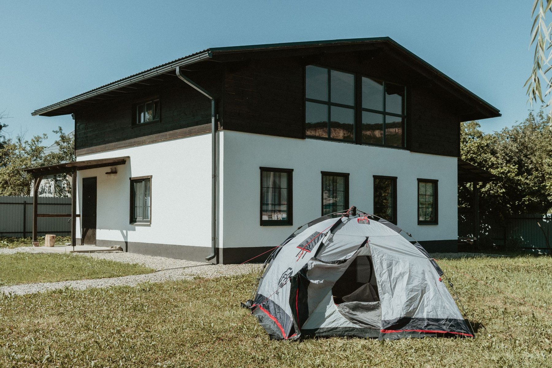 A gray dome tent set up on a grassy lawn in front of a two-story house.