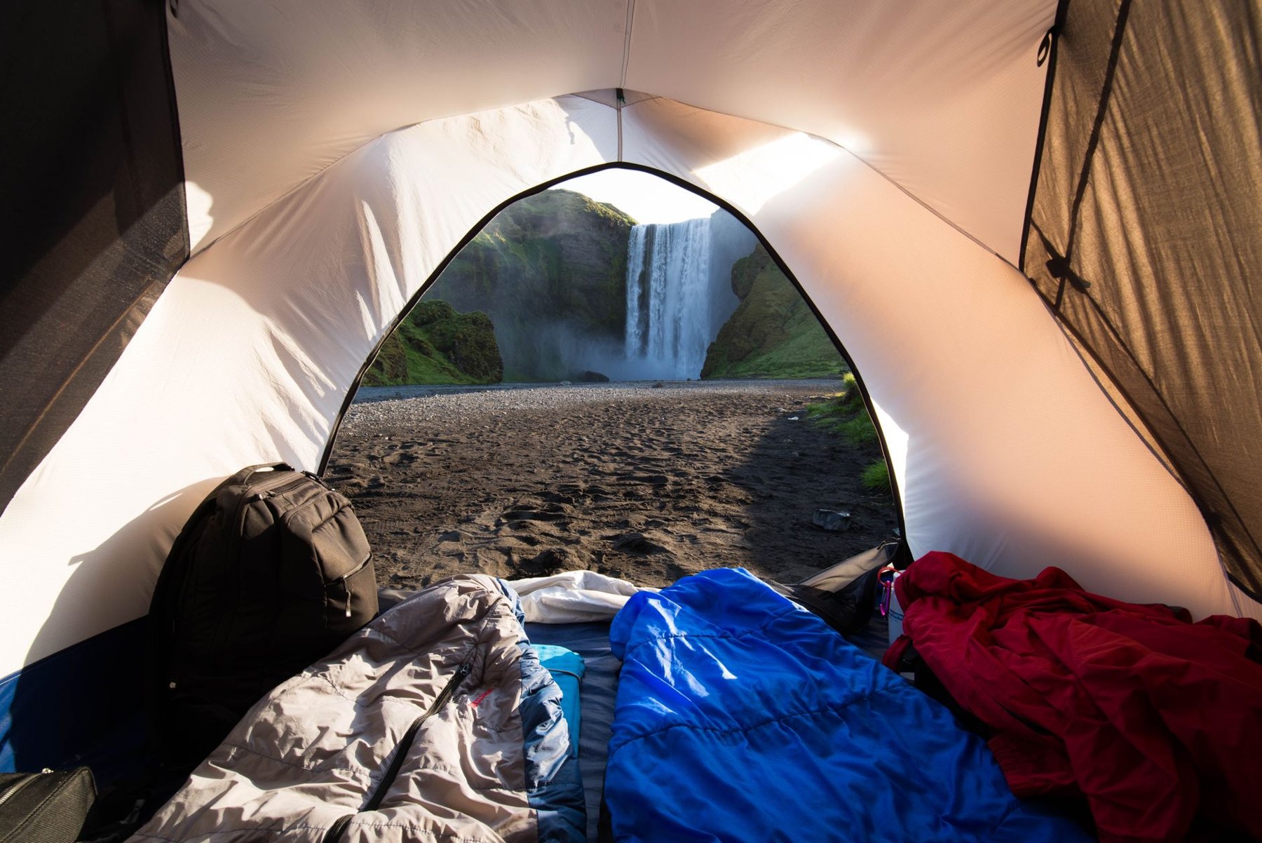 Sleeping bags and a backpack inside a tent with an open doorway overlooking a waterfall.