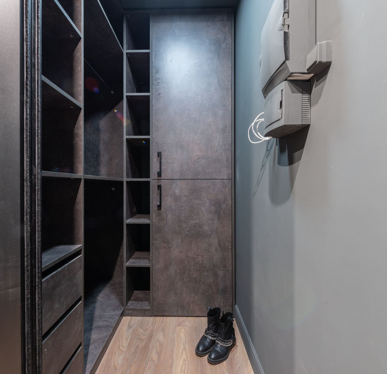 Narrow closet with dark shelves, drawers, a tall cabinet, and boots on the floor.