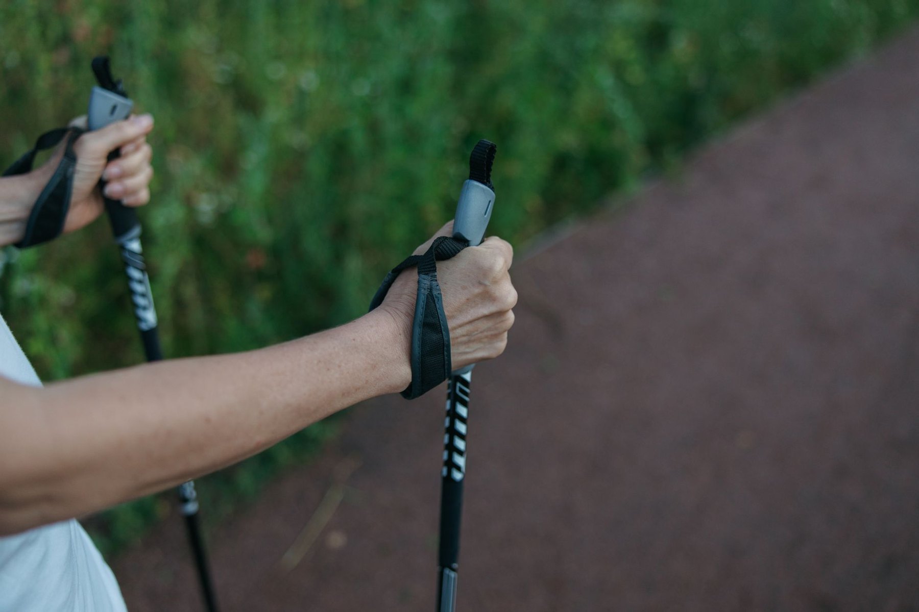 Close-up of hands holding walking pole grips with wrist straps on a trail.